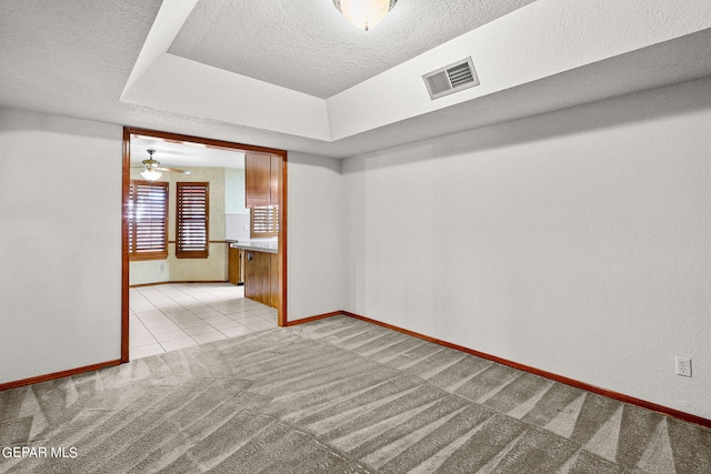 carpeted spare room with a tray ceiling, ceiling fan, and a textured ceiling