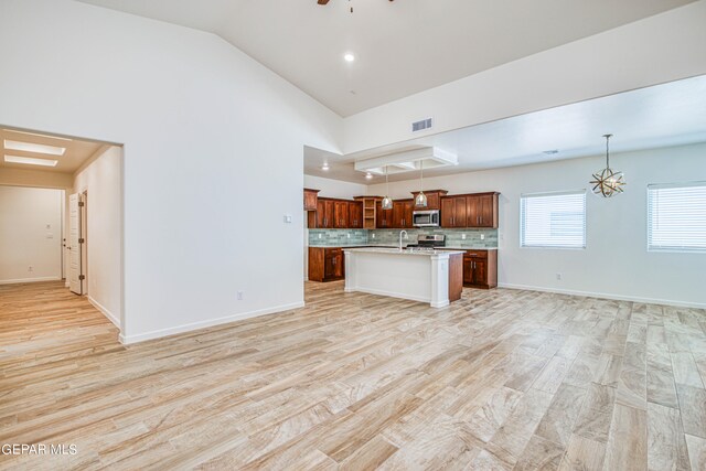 kitchen featuring a center island with sink, light hardwood / wood-style floors, backsplash, and decorative light fixtures