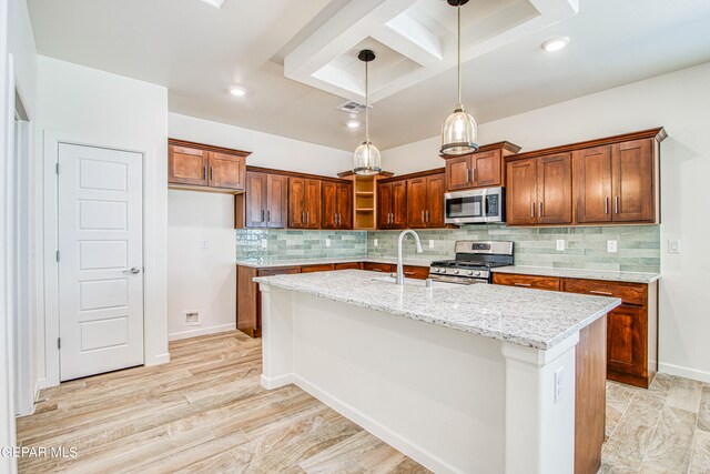 kitchen featuring light stone counters, a center island with sink, appliances with stainless steel finishes, and backsplash