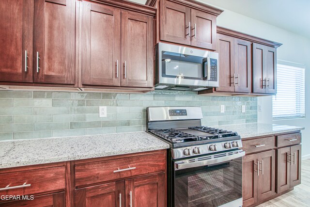 kitchen with appliances with stainless steel finishes, backsplash, light wood-type flooring, and light stone counters