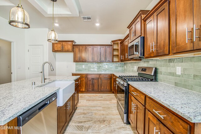 kitchen with light stone countertops, appliances with stainless steel finishes, hanging light fixtures, and sink