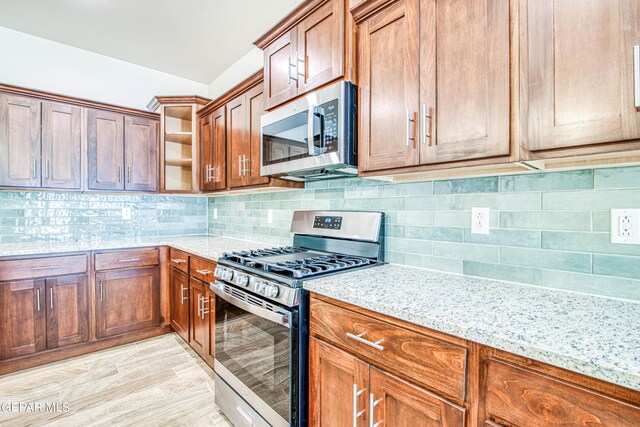 kitchen with appliances with stainless steel finishes, decorative backsplash, light hardwood / wood-style floors, and light stone countertops