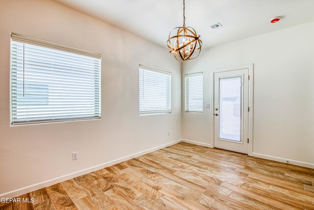 empty room with a notable chandelier, light hardwood / wood-style floors, and a wealth of natural light