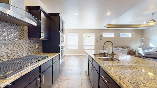 kitchen with decorative light fixtures, sink, a raised ceiling, light stone countertops, and wall chimney exhaust hood