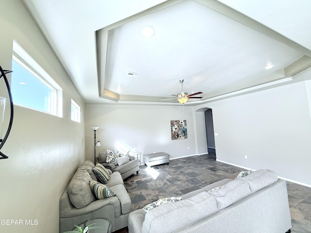 living room featuring a raised ceiling and ceiling fan