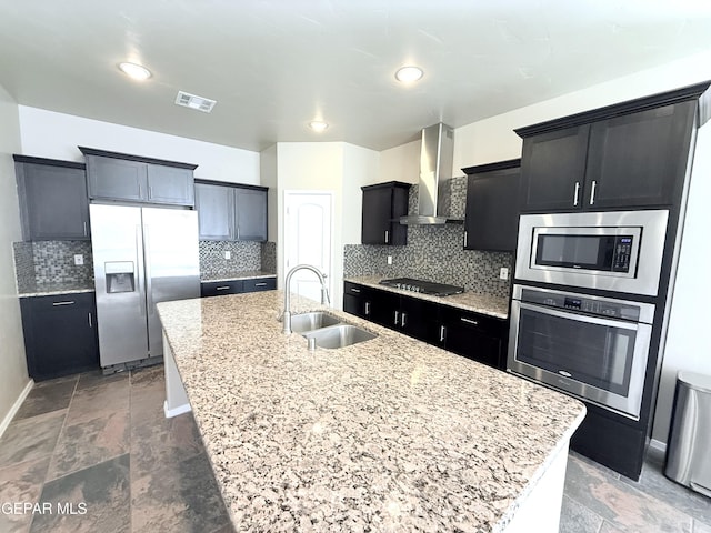 kitchen featuring appliances with stainless steel finishes, sink, backsplash, a kitchen island with sink, and wall chimney exhaust hood