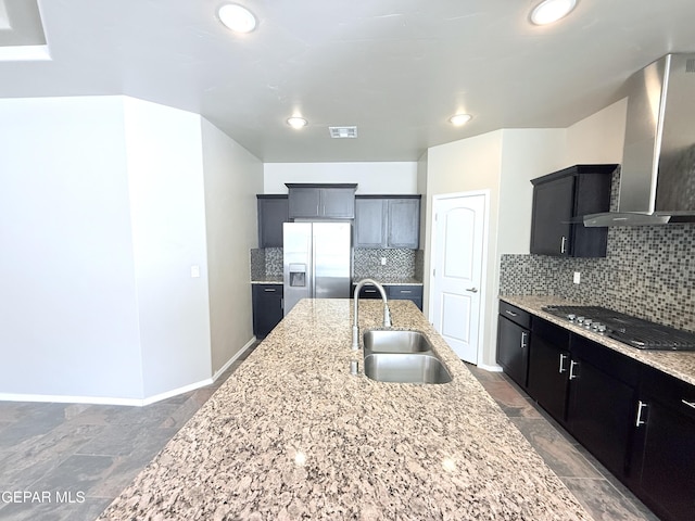 kitchen with stainless steel appliances, light stone countertops, sink, and wall chimney range hood