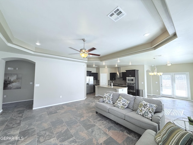 living room with ceiling fan with notable chandelier and a tray ceiling