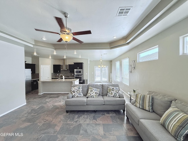 living room with ceiling fan with notable chandelier, a raised ceiling, and sink