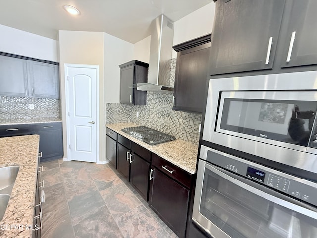 kitchen with wall chimney exhaust hood, stainless steel appliances, light stone countertops, and decorative backsplash