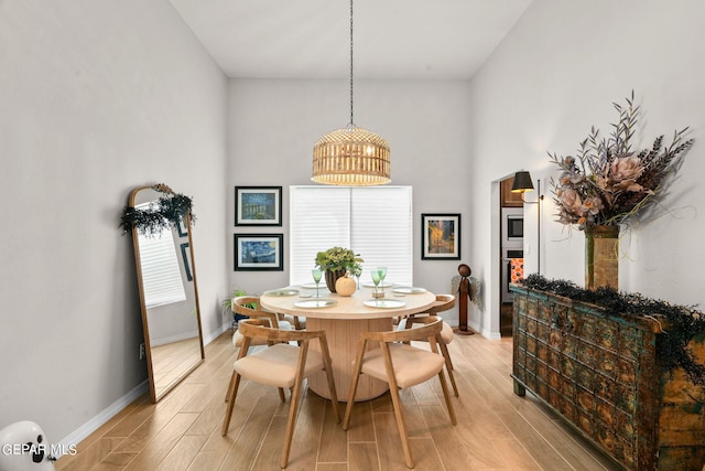 dining area featuring light wood-type flooring and a towering ceiling