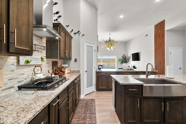 kitchen with sink, wall chimney exhaust hood, stainless steel gas stovetop, light stone countertops, and decorative backsplash