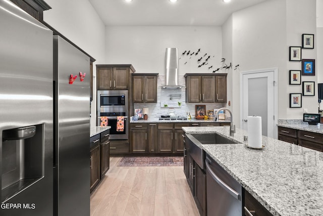 kitchen featuring wall chimney exhaust hood, light stone countertops, appliances with stainless steel finishes, and sink