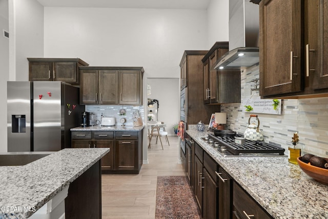 kitchen with wall chimney exhaust hood, decorative backsplash, stainless steel appliances, and dark brown cabinets