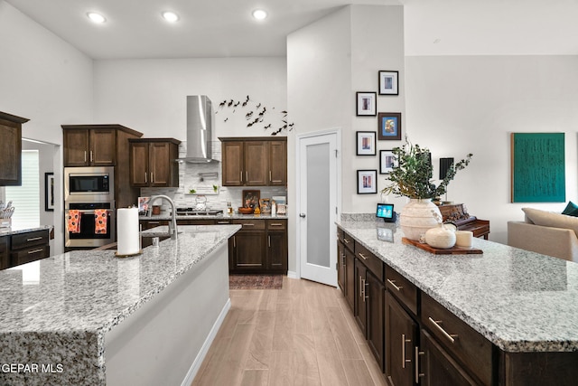 kitchen with wall chimney exhaust hood, light stone countertops, stainless steel appliances, and a spacious island