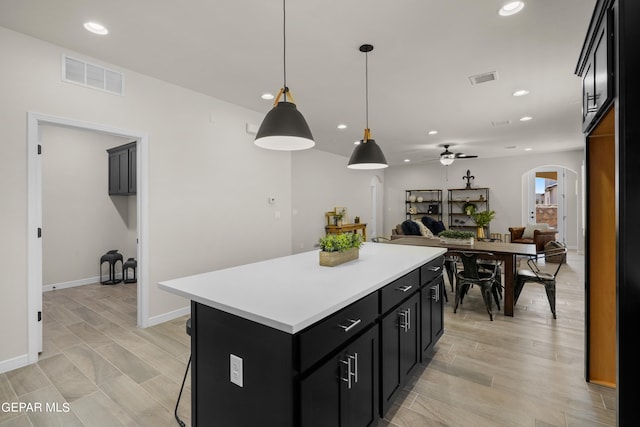 kitchen with pendant lighting, light hardwood / wood-style floors, a center island, a kitchen breakfast bar, and ceiling fan