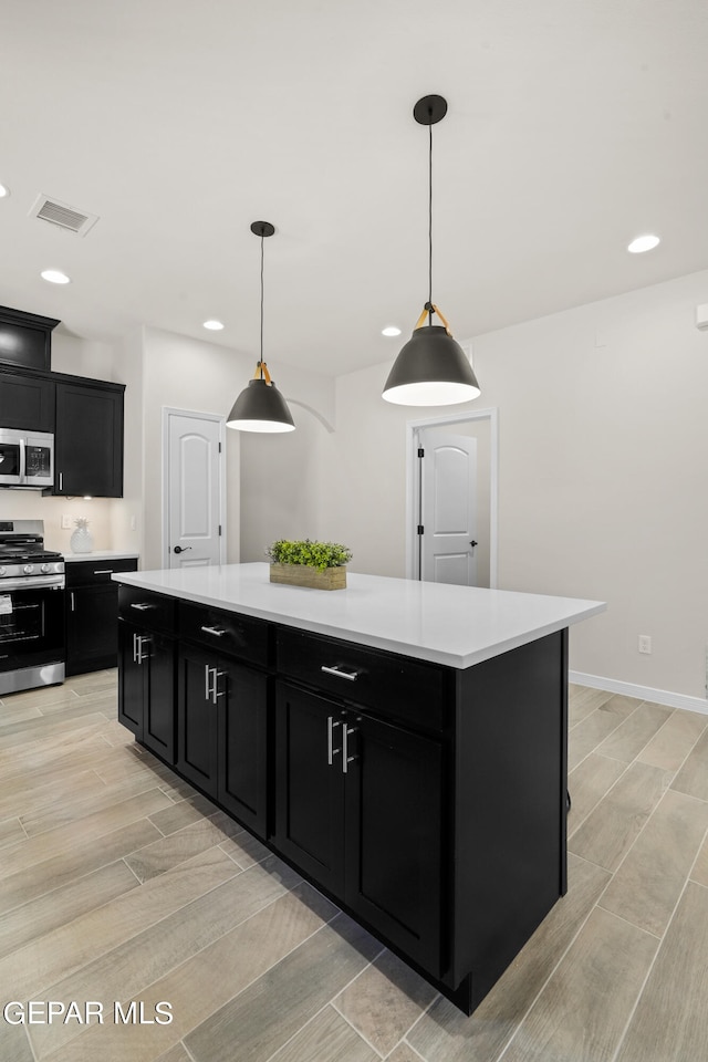 kitchen with decorative light fixtures, appliances with stainless steel finishes, light wood-type flooring, and a kitchen island