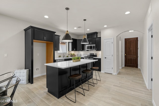 kitchen featuring pendant lighting, sink, a kitchen island, light hardwood / wood-style flooring, and appliances with stainless steel finishes