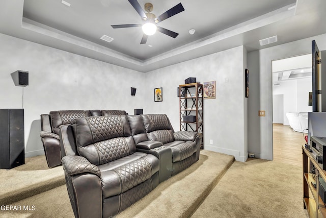 carpeted home theater with ceiling fan and a tray ceiling