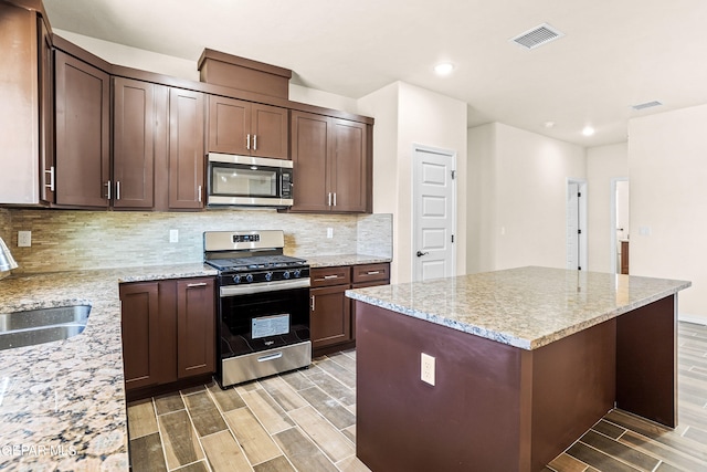 kitchen with appliances with stainless steel finishes, decorative backsplash, light hardwood / wood-style floors, light stone countertops, and a center island