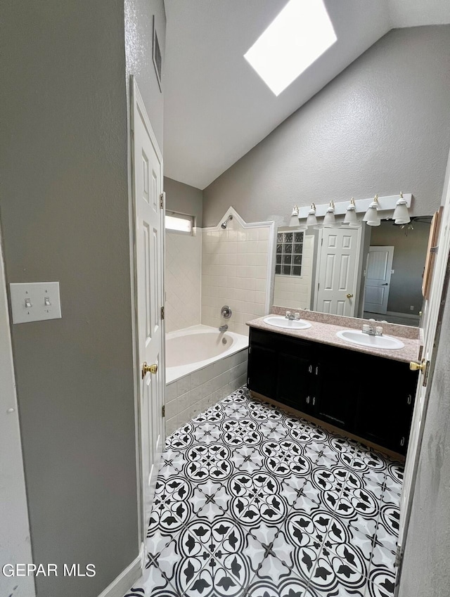 bathroom featuring tiled tub, vaulted ceiling, tile patterned flooring, and vanity