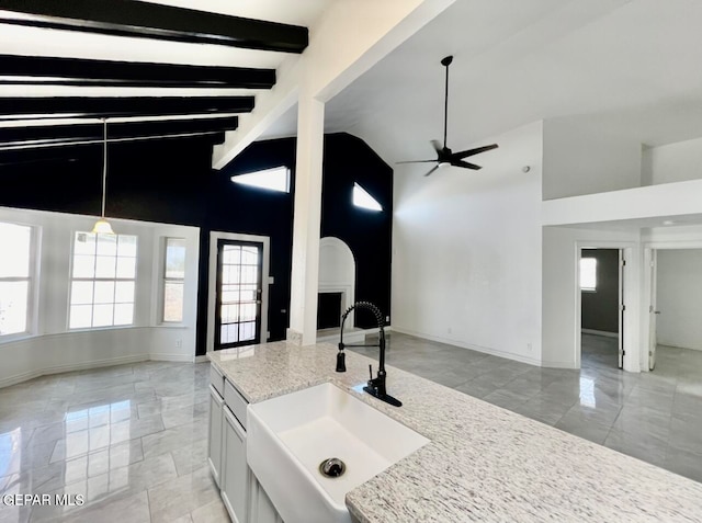 kitchen with pendant lighting, beam ceiling, sink, light stone countertops, and white cabinetry