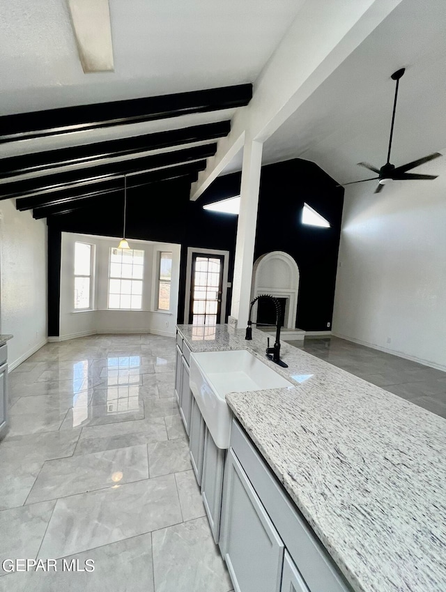 kitchen with gray cabinetry, ceiling fan, sink, light stone counters, and vaulted ceiling with beams