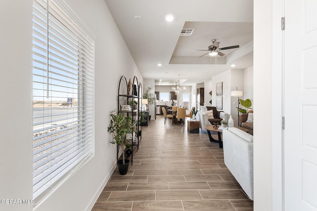 hallway with wood finish floors, recessed lighting, a raised ceiling, visible vents, and an inviting chandelier