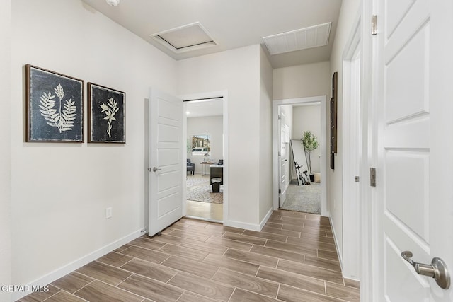 corridor featuring visible vents, baseboards, attic access, and wood tiled floor