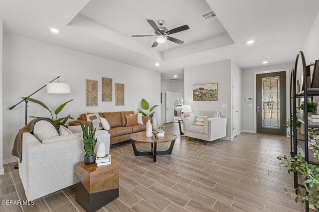 living room featuring a tray ceiling, visible vents, wood tiled floor, ceiling fan, and baseboards