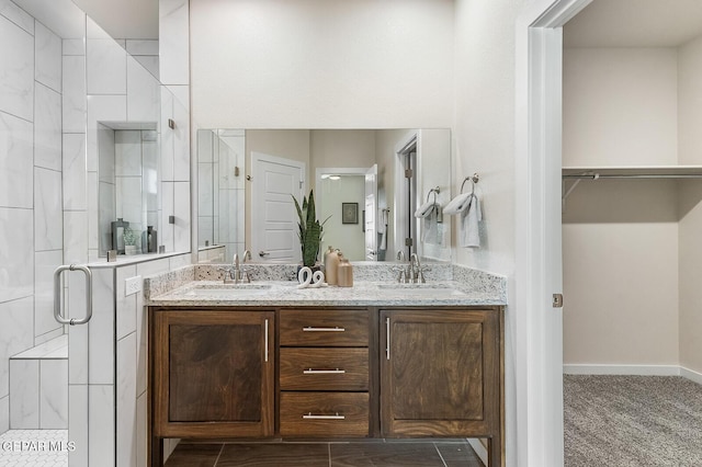 bathroom with double vanity, a spacious closet, a stall shower, and a sink