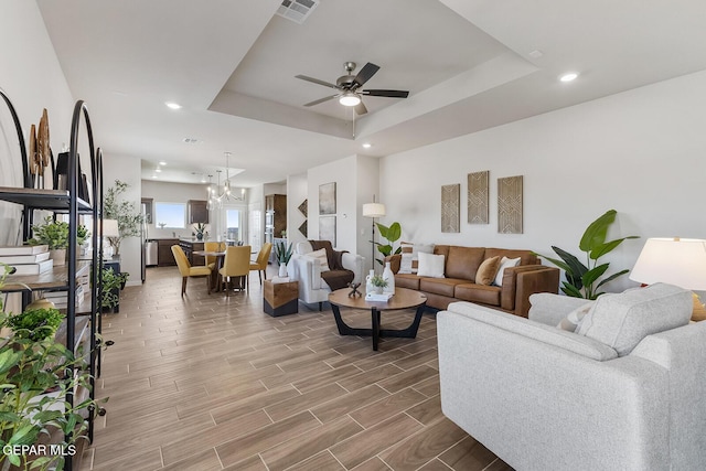 living area with wood tiled floor, visible vents, a raised ceiling, and ceiling fan with notable chandelier