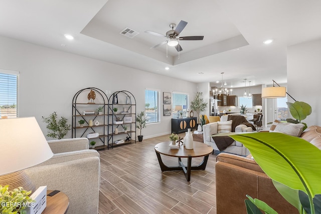 living room with wood finish floors, a raised ceiling, visible vents, and ceiling fan with notable chandelier