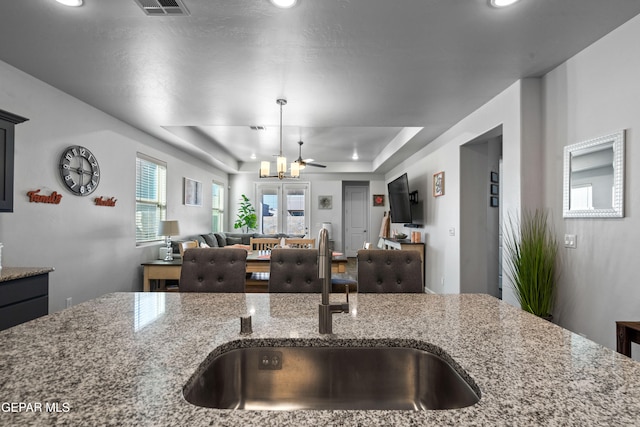 kitchen featuring light stone counters, sink, a raised ceiling, decorative light fixtures, and ceiling fan