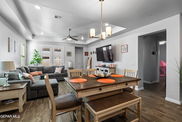 dining space with ceiling fan with notable chandelier, dark hardwood / wood-style floors, and a raised ceiling