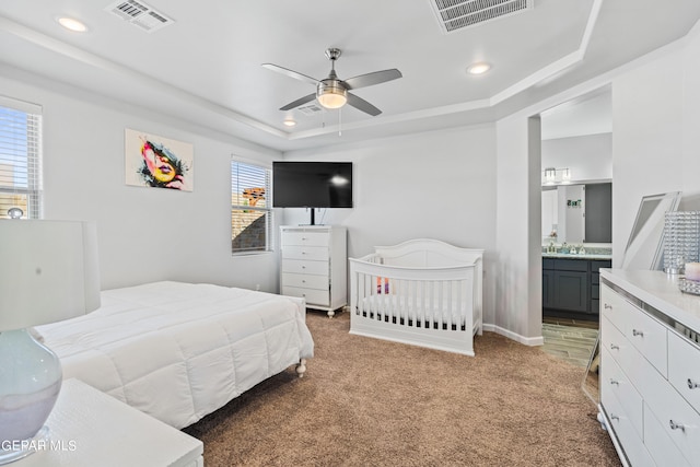 bedroom with ceiling fan, a raised ceiling, ensuite bath, and carpet