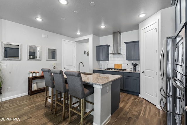 kitchen with sink, wall chimney exhaust hood, a center island with sink, dark hardwood / wood-style flooring, and light stone countertops