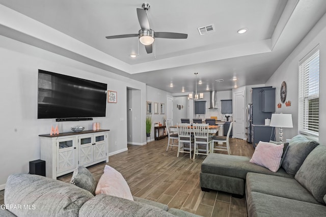 living room with a tray ceiling, ceiling fan, and dark hardwood / wood-style flooring