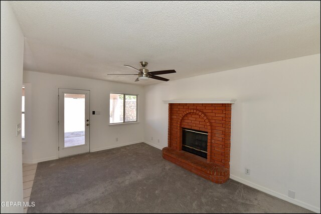 unfurnished living room with dark carpet, a textured ceiling, a fireplace, and ceiling fan