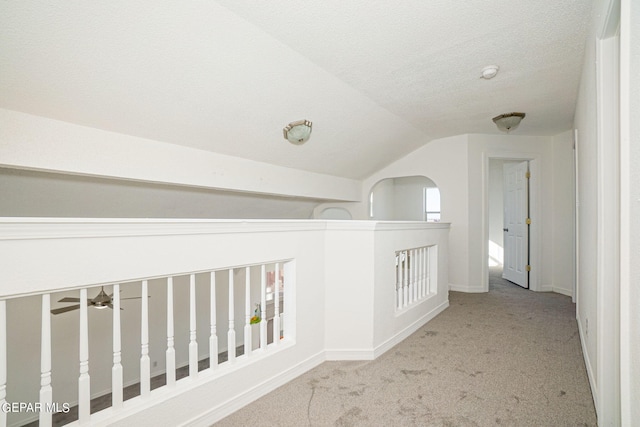 hallway with light carpet, a textured ceiling, and vaulted ceiling