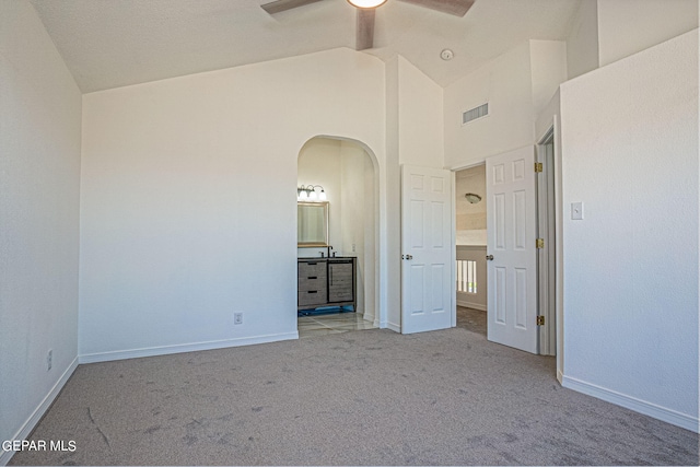 unfurnished bedroom featuring high vaulted ceiling, ensuite bath, ceiling fan, and light colored carpet