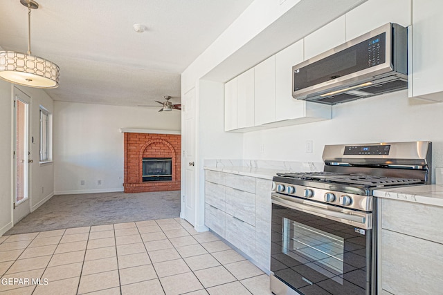 kitchen featuring ceiling fan, white cabinets, a brick fireplace, appliances with stainless steel finishes, and light carpet