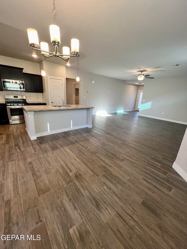 kitchen featuring appliances with stainless steel finishes, hanging light fixtures, light stone counters, a kitchen island with sink, and dark hardwood / wood-style floors