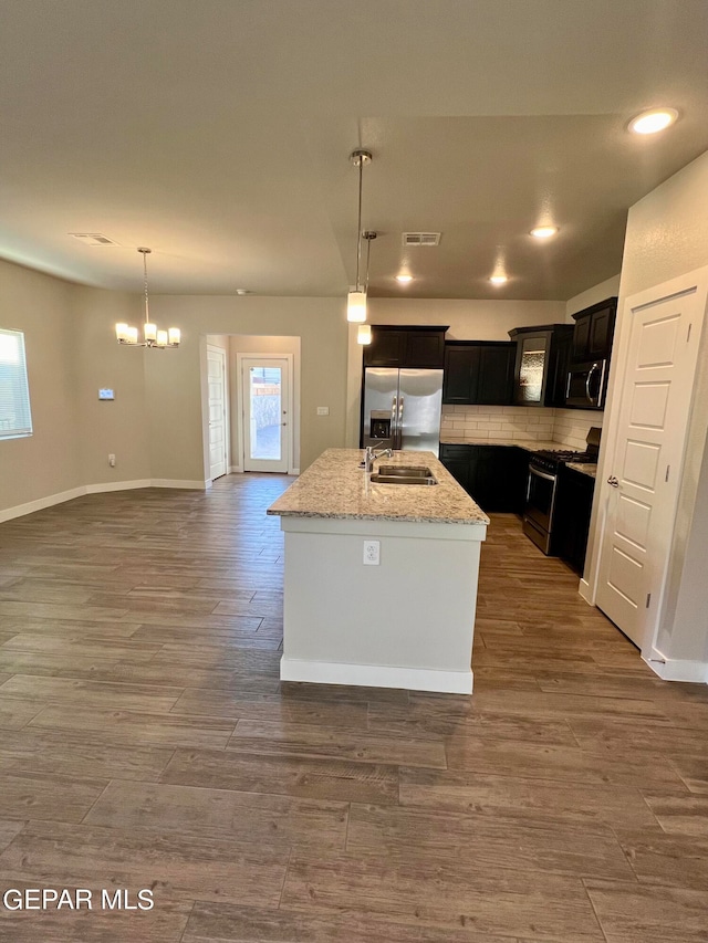 kitchen with a kitchen island with sink, sink, an inviting chandelier, stainless steel appliances, and dark hardwood / wood-style flooring