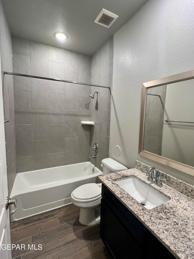 full bathroom featuring wood-type flooring, a textured ceiling, tiled shower / bath, vanity, and toilet