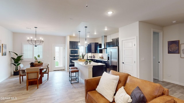 kitchen with appliances with stainless steel finishes, hanging light fixtures, an island with sink, wall chimney exhaust hood, and a breakfast bar area