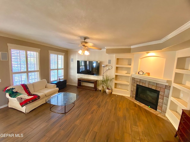 living room featuring built in shelves, ornamental molding, ceiling fan, a tiled fireplace, and hardwood / wood-style floors