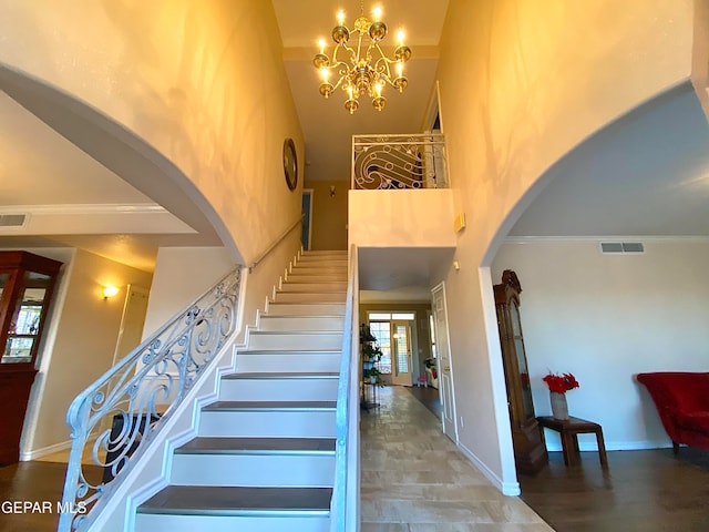 staircase with ornamental molding, a chandelier, and a high ceiling