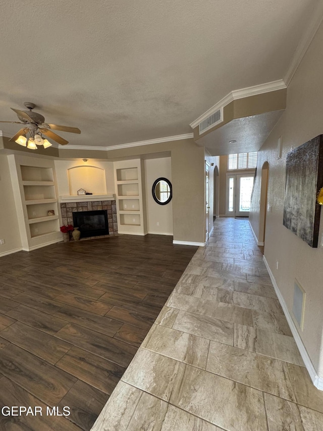 unfurnished living room with crown molding, a fireplace, built in features, and a textured ceiling