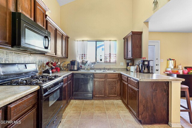 kitchen featuring light countertops, a kitchen breakfast bar, a peninsula, a towering ceiling, and black appliances